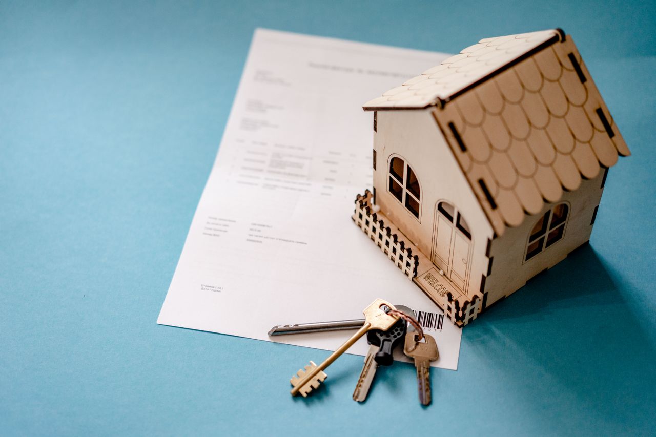 hero-02 Miniature wooden house with keys and contract symbolizing real estate transactions.