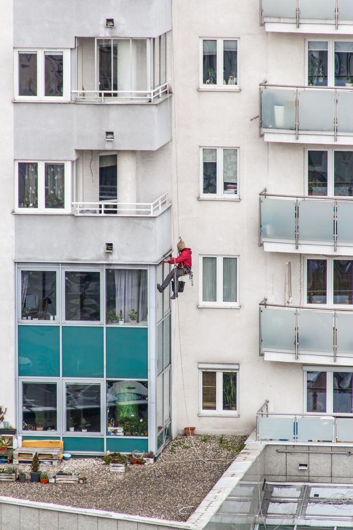why-choose-us-02 Professional window cleaner scaling a modern residential building with glass balconies.