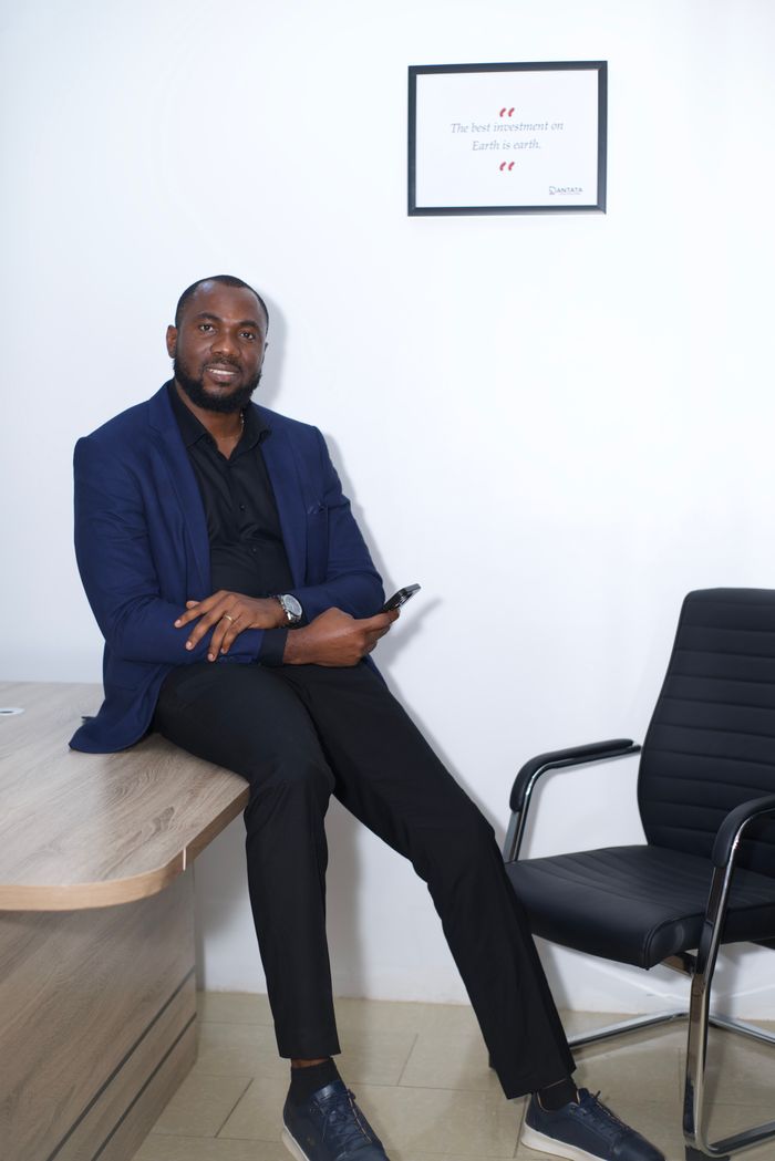 about-01 Confident businessman seated on a desk in a modern office, holding a phone.