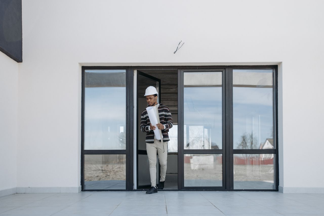 services-01 A professional architect walks out of a modern building holding house plans, symbolizing construction and development.