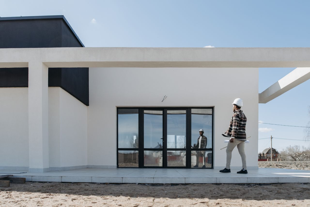 services-01 Architect with hard hat evaluating modern house exterior. Ideal for construction and architecture themes.
