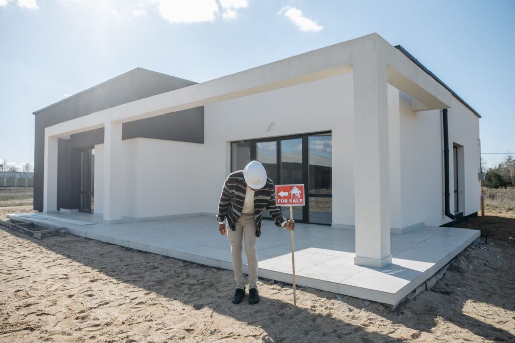 services-09 Real estate agent with hard hat standing by a modern house for sale.