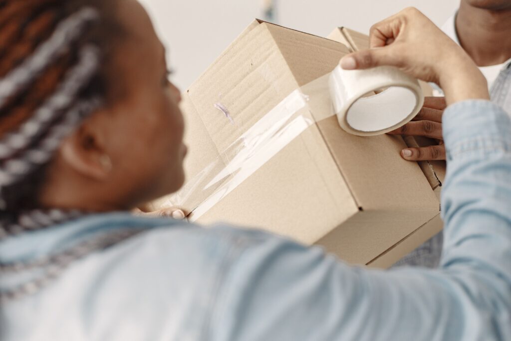 Close-up of people sealing a cardboard box with tape during moving preparations.