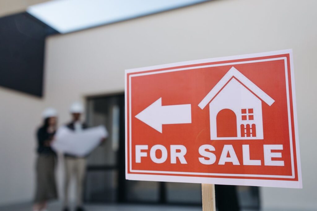 Mastering the First Impression: Your intriguing post title goes here A real estate sign indicates a property for sale as two agents in hard hats discuss building plans outdoors.